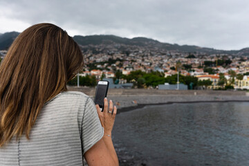 A young woman uses her smart phone. In the background mountains and sea.