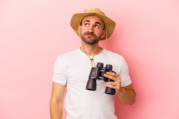 Young caucasian bald man holding binoculars isolated on pink background  dreaming of achieving goals and purposes