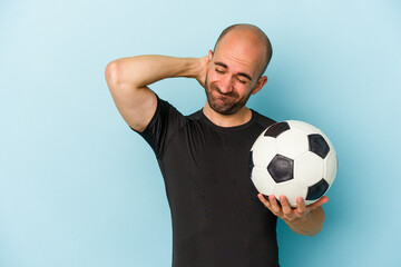 Young business bald man playing football isolated on blue background  touching back of head, thinking and making a choice. - obrazy, fototapety, plakaty
