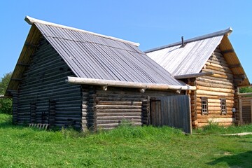 Wooden house made of logs, green grass on a clear day. An old Russian rustic wooden house of the 19th century