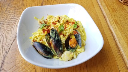 Pasta with cheese and large mussels in a white plate on the table