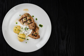 Grilled pork meat with mushroom sauce and potato on white plate on wooden black background