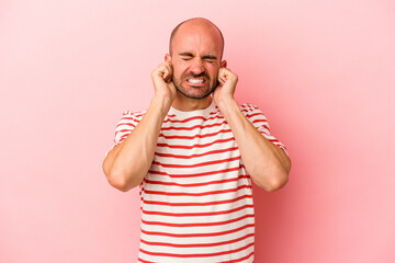 Fototapeta premium Young caucasian bald man isolated on pink background covering ears with hands.
