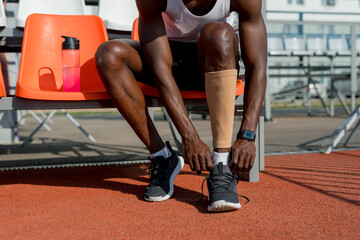 An African American male track and field athlete is sitting on a bench wearing a sports stocking on his left leg before the race