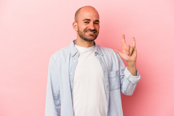 Young caucasian bald man isolated on pink background  showing a horns gesture as a revolution concept.