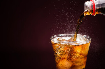 Pour sparkling water in a cola glass with ice cubes. on a dark black background.