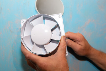 Fototapeta premium Man is installing the wall bathroom fan vent. Restoration process. Wires in hands. Maintenance repair works renovation in the flat.