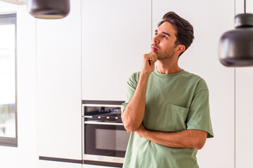 Young mixed race man in his kitchen looking sideways with doubtful and skeptical expression.
