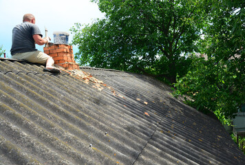 Brick chimney repair. A roofer on an asbestos roof is replacing cracked bricks, building a new brick chimney.