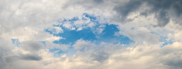 A piece of blue sky can be seen through the light and dark clouds. Blue sky surrounded by clouds