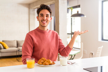 Young mixed race man having breakfast in a kitchen on the morning showing a copy space on a palm and holding another hand on waist.