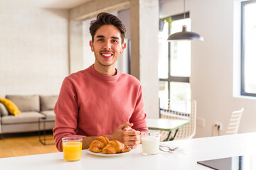 Fototapeta na wymiar Young mixed race man having breakfast in a kitchen on the morning happy, smiling and cheerful.