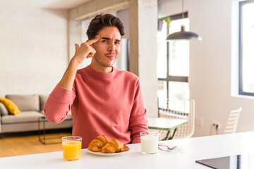 Fototapeta na wymiar Young mixed race man having breakfast in a kitchen on the morning pointing temple with finger, thinking, focused on a task.