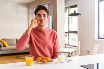 Fototapeta na wymiar Young mixed race man having breakfast in a kitchen on the morning with fingers on lips keeping a secret.