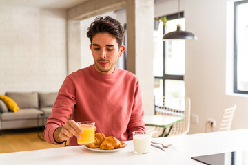 Fototapeta na wymiar Young mixed race man eating croissant in a kitchen on the morning