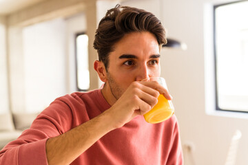 Young mixed race man drinking orange juice in his kitchen