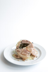 Braised pork on a white plate with bay leaves, white background