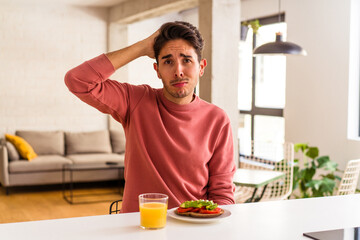Fototapeta na wymiar Young mixed race man having breakfast in his kitchen being shocked, she has remembered important meeting.