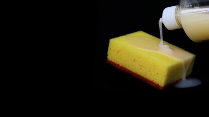 yellow dish sponge, liquid soap is poured on the sponge, black background