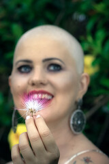 Portrait Beautiful and strong bald woman fighting breast cancer. Happy and looking intent and steady. holding flowers. Hairless. Green eyes