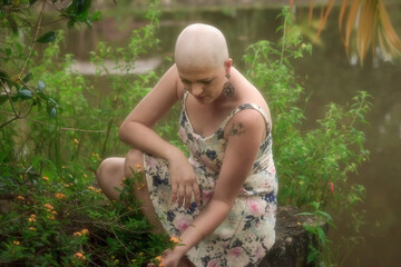 Beautiful and strong bald woman fighting breast cancer Thoughtful and happy. in the middle of the flowers. Hairless. Calm. Sensual flower print dress.