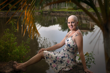 Beautiful and strong woman fighting breast cancer Smiling and happy. Hairless and bald. live and joy of fighting. Flower print dress on the lake and on the ranch.