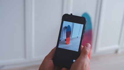 Caucasian Male Using Smartphone to Take Photo of Skateboard to Sell It During Online Garage Sale to Earn Extra Money	