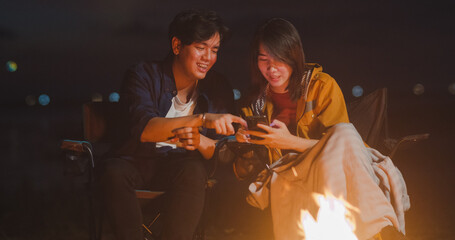 Young asia couple backpackers enjoying in camping at night near campfire on beach. Male and female...