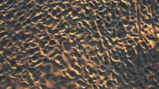 Bird's-eye view of a sandy relief beach. The drone is flying over the trampled sand, the camera moves from top to bottom. Aerial photography from top to bottom, a top-down panorama captured by a