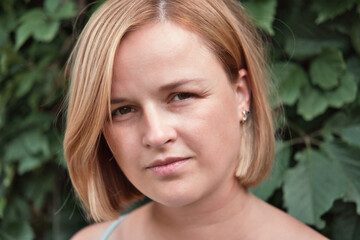 Close-up portrait of beautiful young woman against tropical green leaves background. Serious attractive caucasian woman.