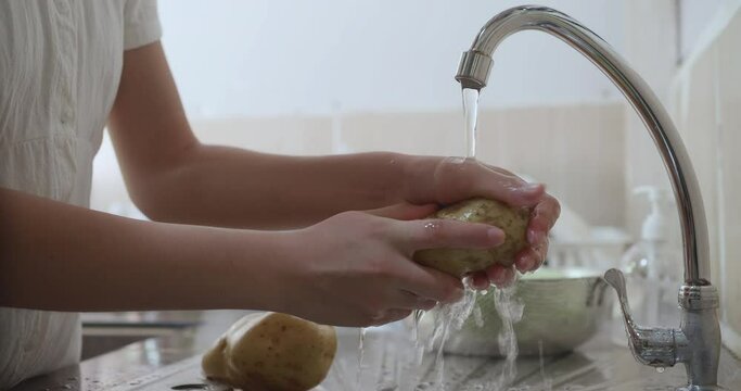 Female hands washing collards under running stream of water in sink at kitchen
