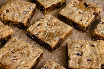 Brown Butter Bourbon Pecan Chocolate Chunk Blondies Garnished with Flaky Sea Salt: Blondies cut into squares and served on a dark wood cutting board