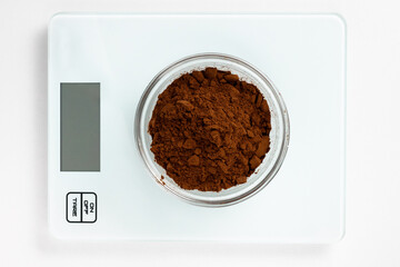 Cocoa powder is poured into a measuring bowl and placed on the scales. Close-up, top view.