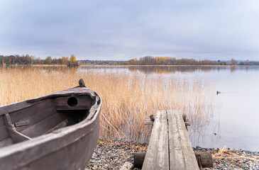Obraz premium Old wooden boat on the shore of beautiful misty lake and autumn forest landscape. Autumn forest and lake background. Great design for any purposes.