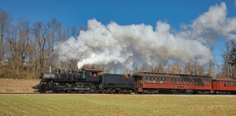Obraz na płótnie Canvas View of an Antique Restored Steam Passenger Train Blowing Smoke and Steam on a Sunny Winter Day