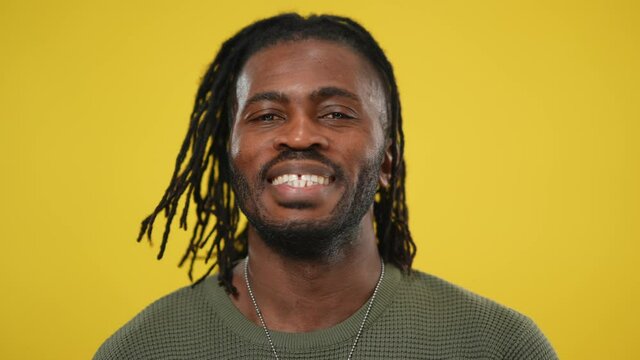 Headshot of cheerful African American handsome man shaking dreadlocks on head smiling looking at camera. Close-up portrait of positive confident guy posing at yellow background
