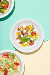 Greek salad in white plate hard shadows on blue and yellow