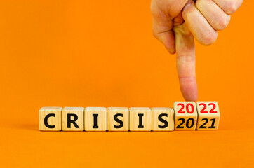 2022 crisis and new year symbol. Businessman turns wooden cubes and changes words 'crisis 2021' to 'crisis 2022'. Beautiful orange background, copy space. Business, 2022 crisis and new year concept.
