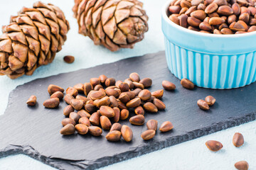 A handful of unpeeled pine nuts on a slate board, pine cones and nuts in a bowl. Detox and cure for insomnia. Healthy vitamin nutrition