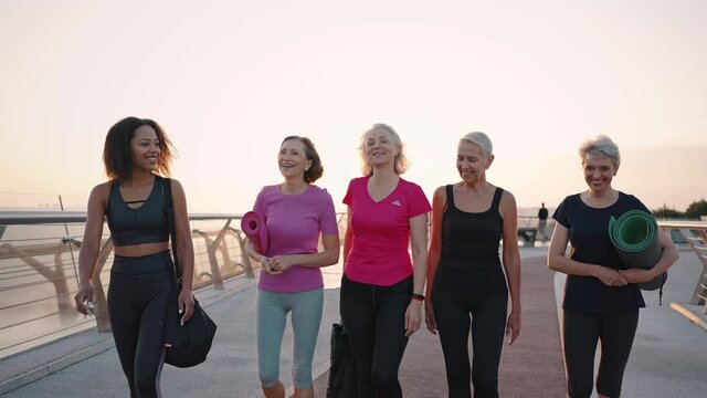 Active aging concept. Group of positive mature women walking with coach to outdoor training, talking and laughing