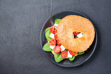 Appetizing ready-to-eat bagels stuffed with tomatoes, feta and spinach leaves on a plate on a black...