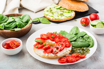 Delicious bagel stuffed with feta, tomatoes and pumpkin seeds and spinach leaves on a plate. Light Healthy Vitamin Snack