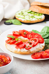Delicious bagel stuffed with feta, tomatoes and pumpkin seeds and spinach leaves on a plate. Light Healthy Vitamin Snack. Vertical view. Close-up