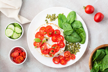 Delicious bagel stuffed with feta, tomatoes and pumpkin seeds and spinach leaves on a plate. Light Healthy Vitamin Snack. Top view