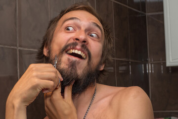A bearded man trims his beard with small scissors
