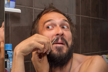 A man with a beard does hair removal inside his nose