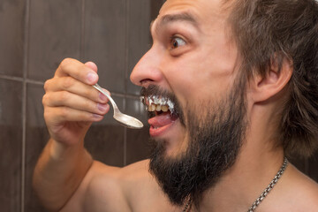 A bearded man eats sour cream while smearing his mustache with it
