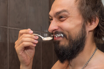 A bearded man eats sour cream while smearing his mustache with it