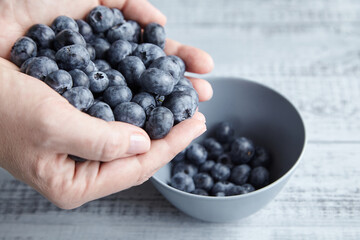 A handful of blueberries and bowl on wooden background