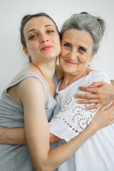 Happy senior mother is hugging her adult daughter, the women are laughing together, sincere family of different age generations having fun on white background, mothers day.